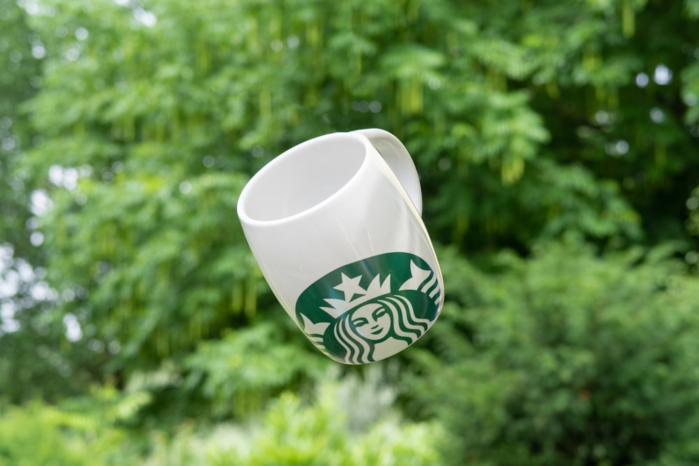 selective focus photography of floating white and green Star Bucks ceramic mug