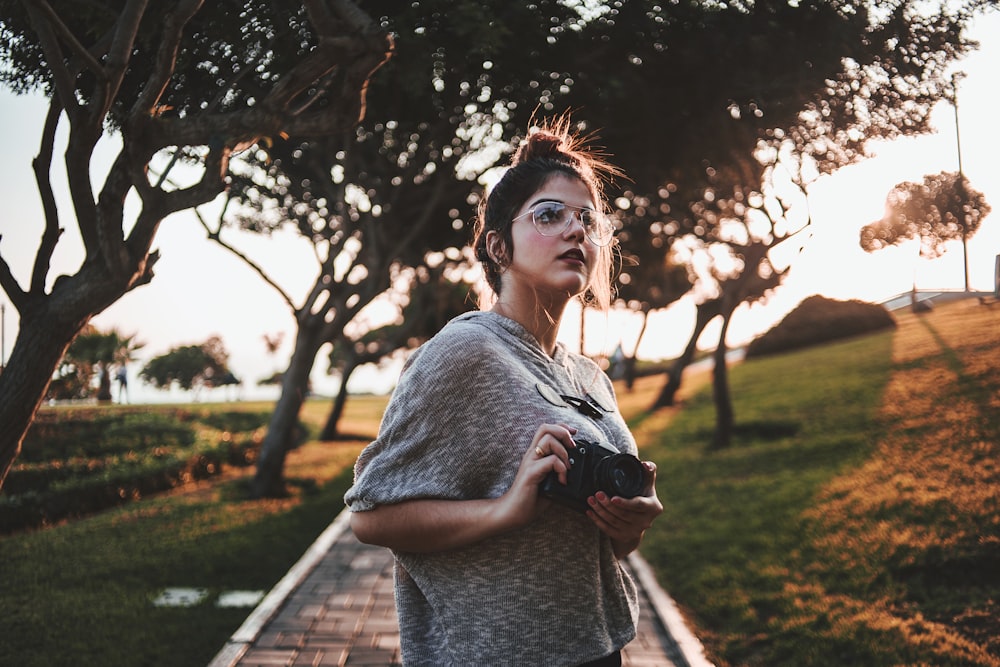 woman standing holding camera near tree