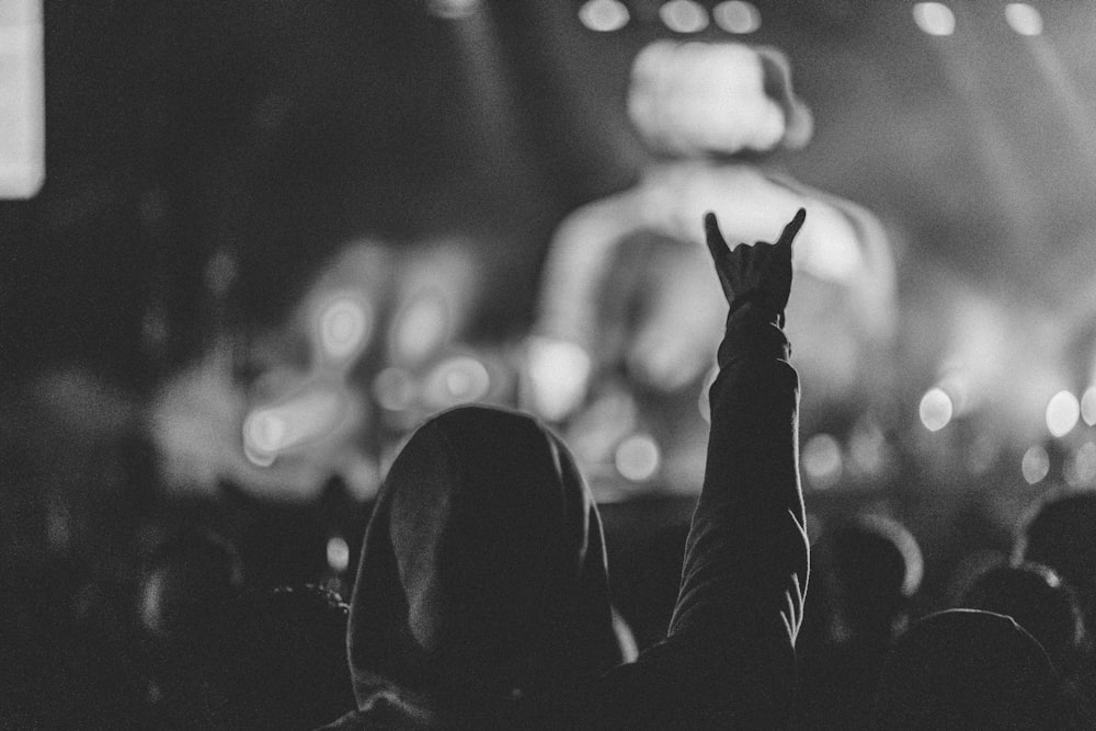 Foto in scala di grigi di una persona in felpa con cappuccio che guarda un concerto