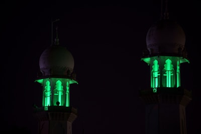 Nighttime view of illuminated minarets against a dark green sky.