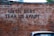 A brick wall has the phrase 'UNTIL DEBT TEAR US APART' spray-painted in black. A section of a parked car is visible at the bottom of the image, adding a touch of urban life.