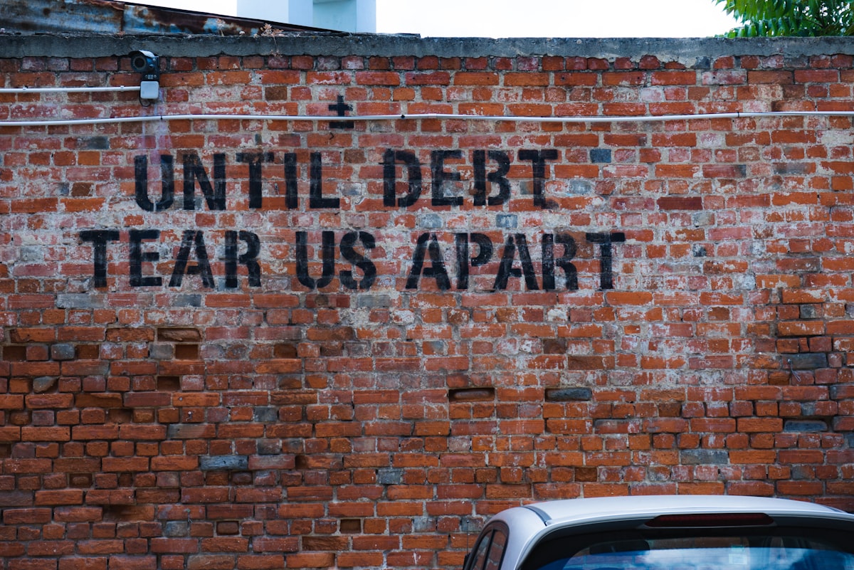 Brick wall with painted graffiti reading Until Debt Tear Us Apart symbolizing the burden of financial debt