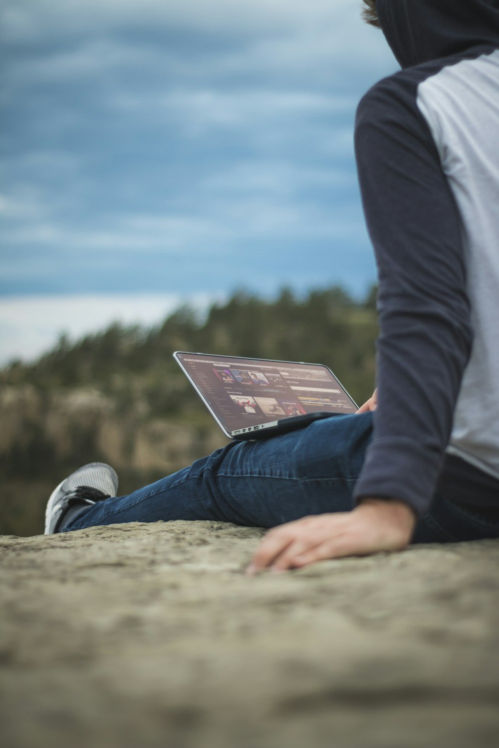 man sitting on cliff with laptop on legs