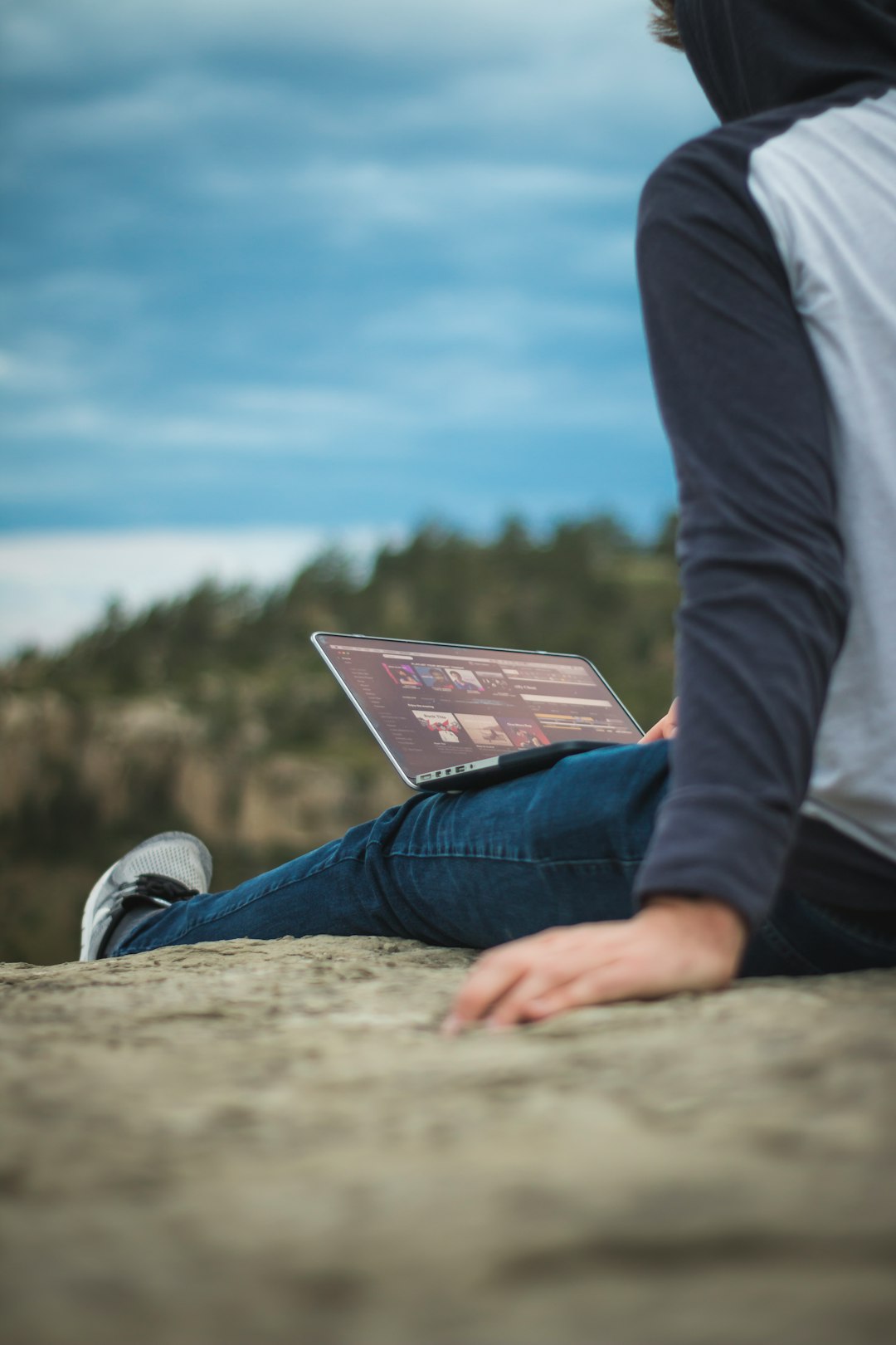 man sitting on cliff with laptop on legs