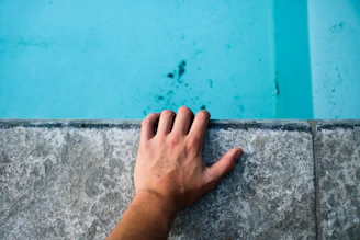 person's left hand holding gray concrete surface
