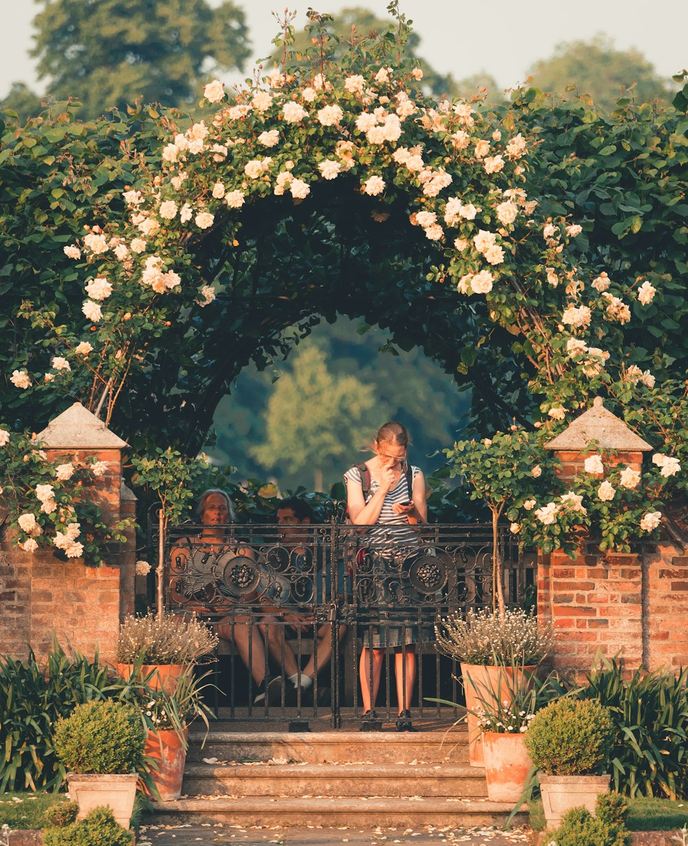 woman standing on gray fence under arch-shade flower plant at daytime