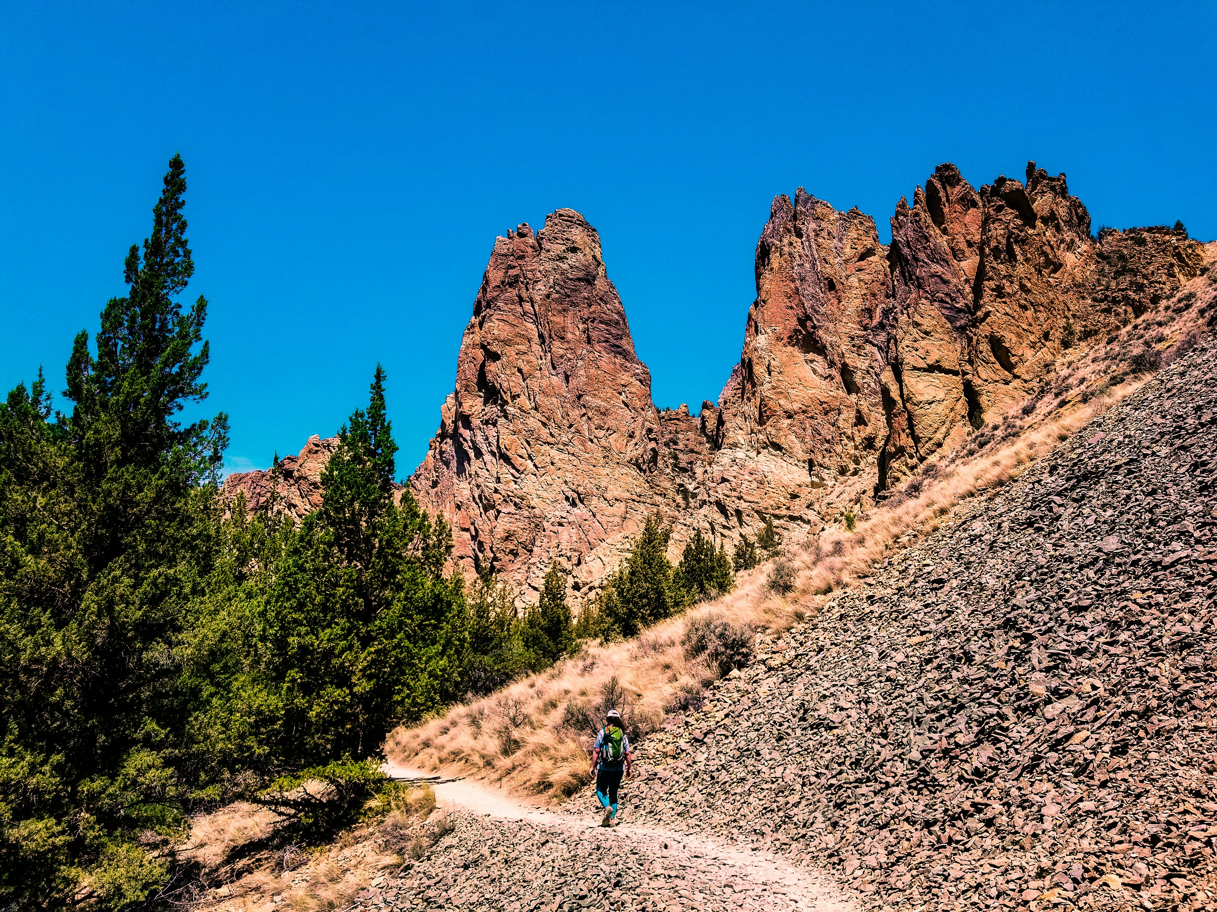 man walking on mountain pathway under clear sky