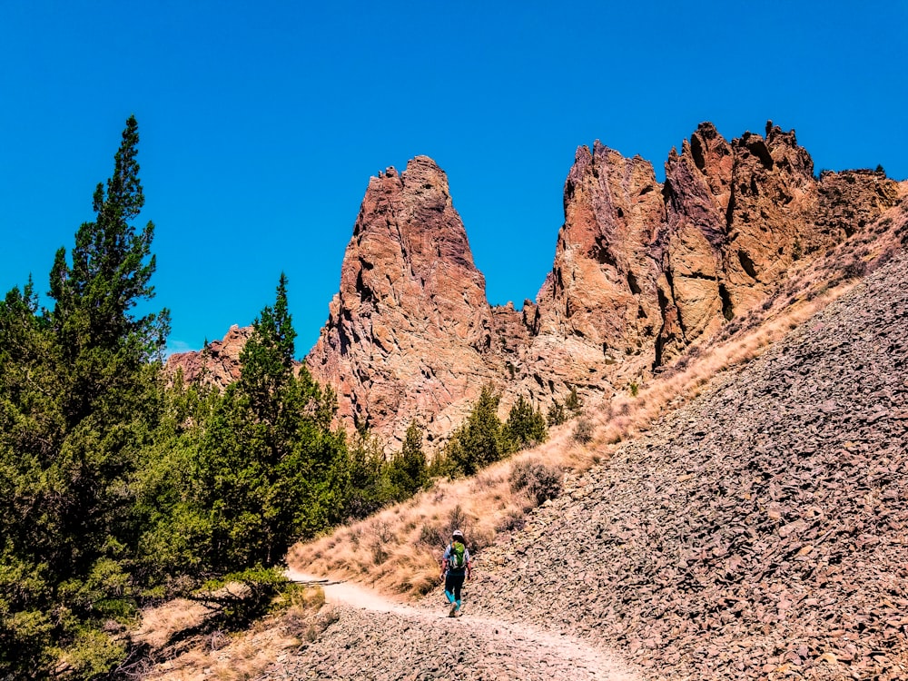 man walking on mountain pathway under clear sky