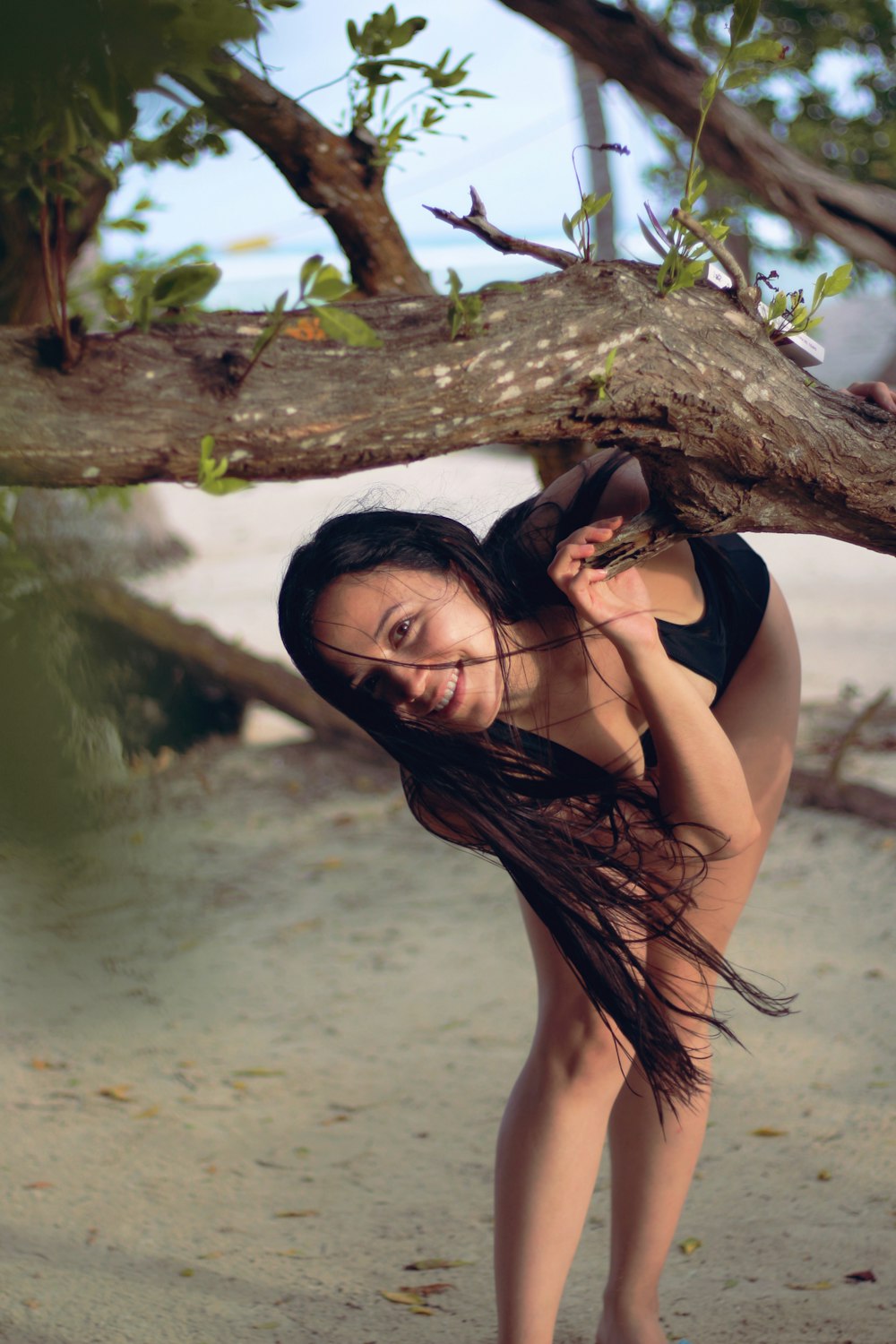 a woman standing next to a tree on a beach