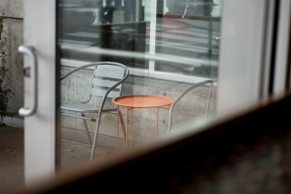 灰色の金属製の椅子の横の丸いオレンジ色の金属製のテーブル