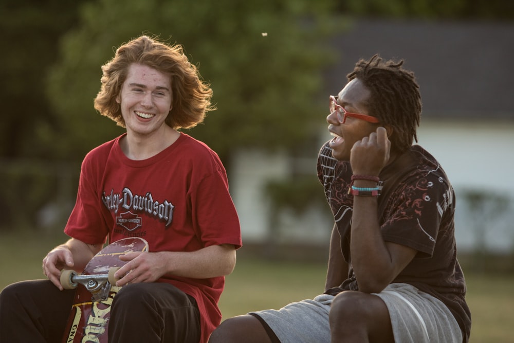 man holding skateboard sitting next to man during daytime