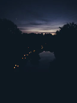 A serene night lake scene with rectangular paper lanterns gently floating on the water, reflecting soft purple and warm gold hues