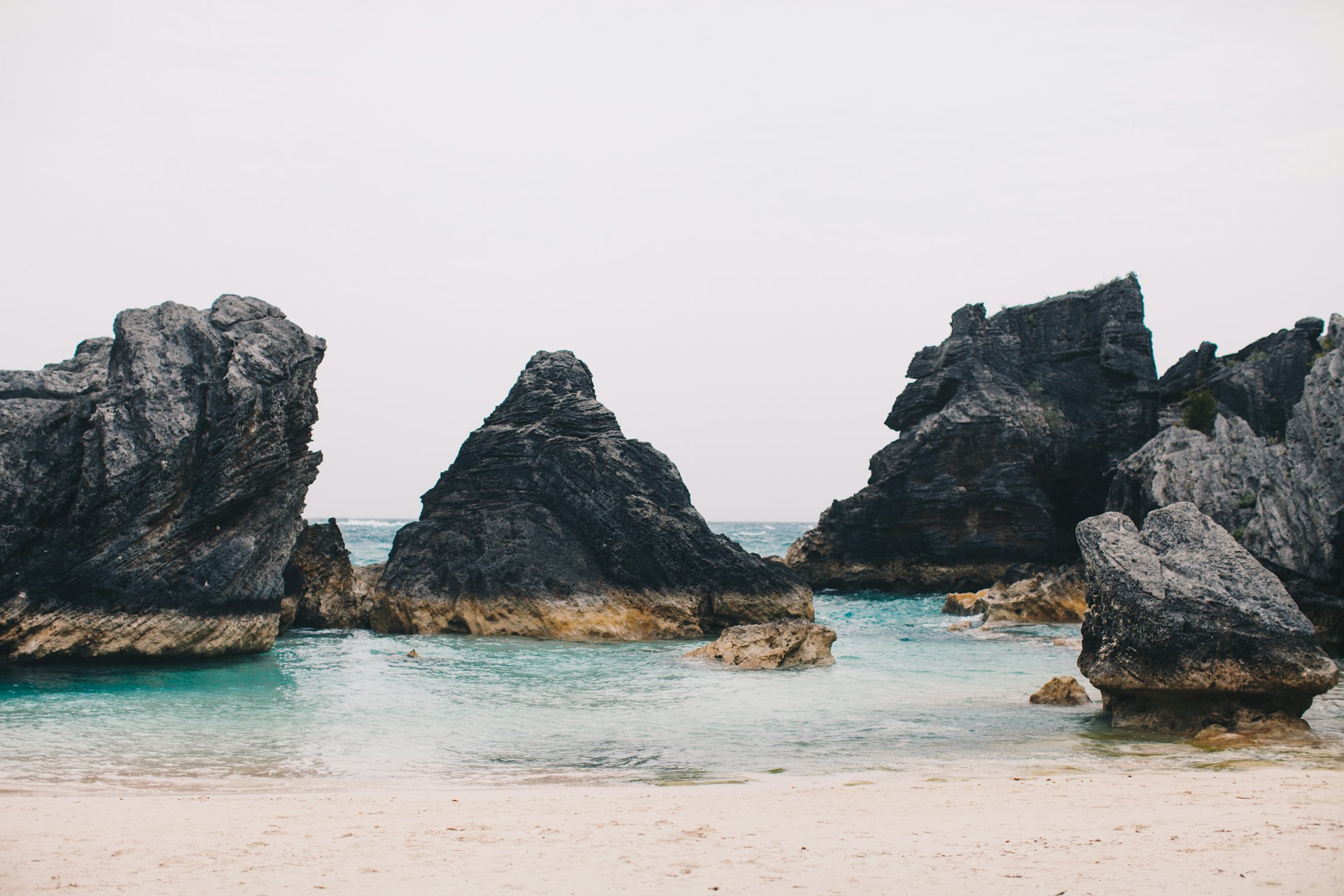 Dark limestone rock formations framing a pink sand cove on Bermuda's south shore