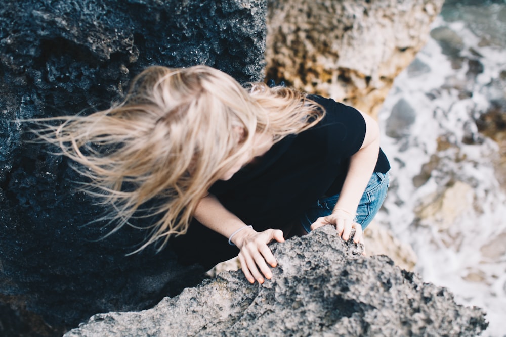 woman climbing on cliff near body of water