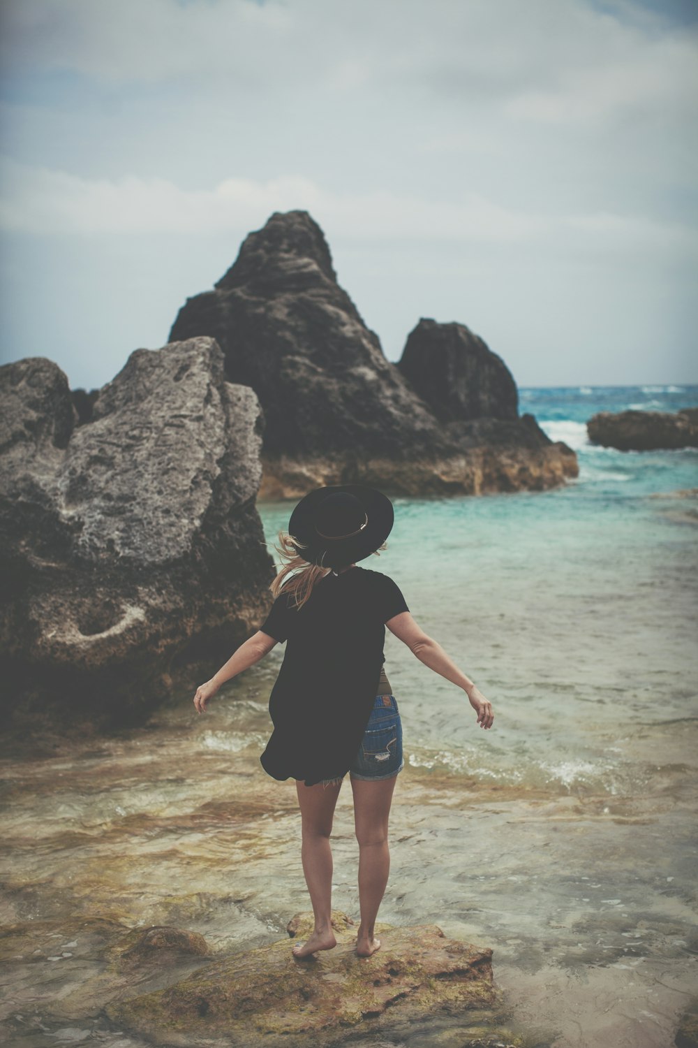 woman standing on rock near ocean shoreline
