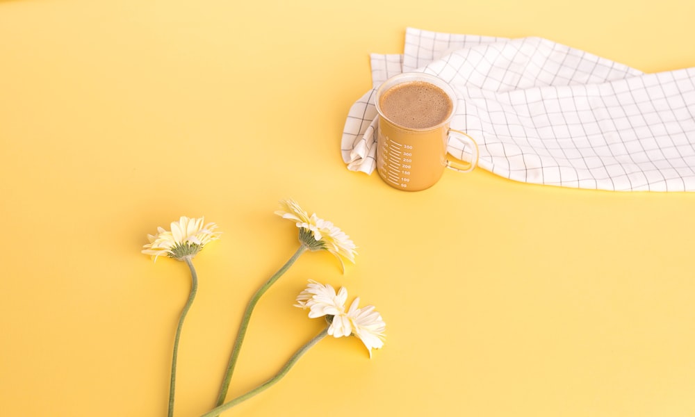 white flowers near clear glass mug on yellow table