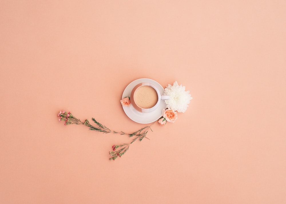 a cup of coffee on a saucer next to flowers