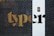 A metal security gate with a hexagonal pattern is placed in front of a building wall. Bright yellow and black letters are partially visible behind the gate. A white section of the wall features a black intercom panel near the top.