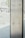 A glass panel stands vertically, featuring two round fasteners visible on the metallic surface. Letters are scattered on the glass, creating an abstract design. The background is blurred, showcasing a set of steps and indistinct structures.