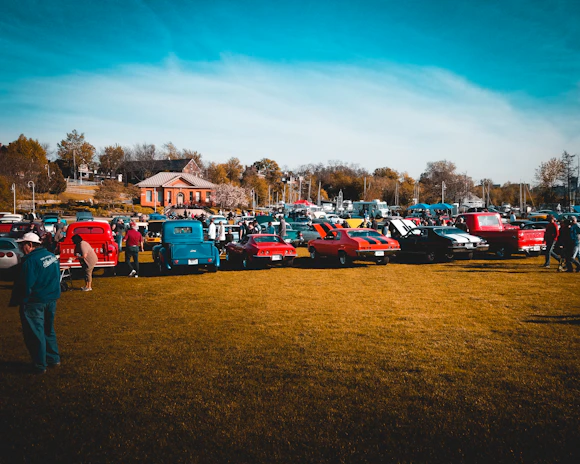 A group of friends sitting on picnic blankets enjoying food from trucks while classic cars shine nearby.