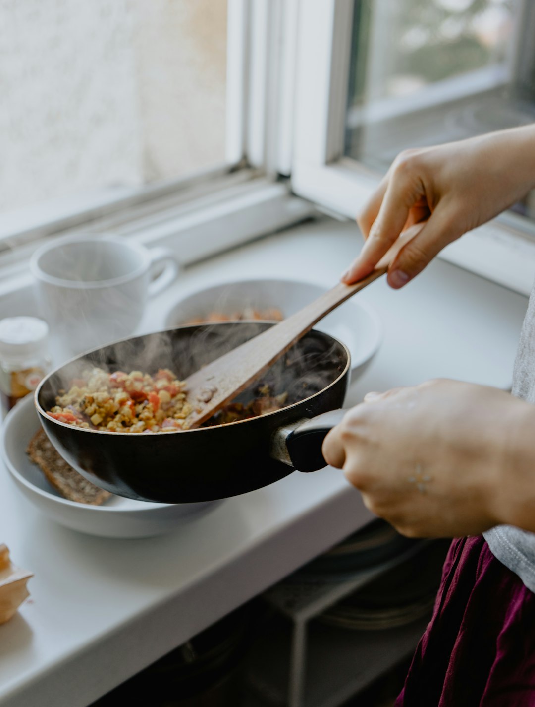 person holding black frying pan serving food into a bowl.