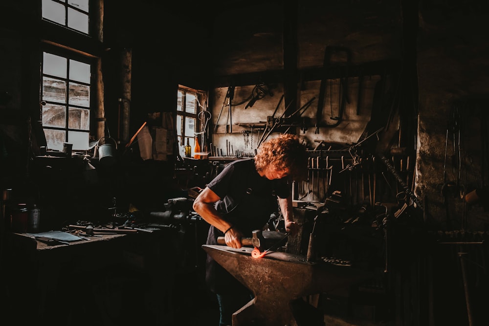 man holding hammer while forging on anvil inside room