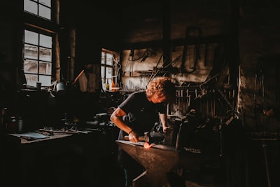 man holding hammer while forging on anvil inside room craft google meet background