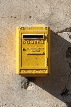 yellow steel mail box mounted on gray wall