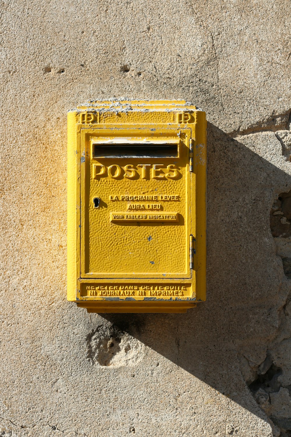 yellow steel mail box mounted on gray wall