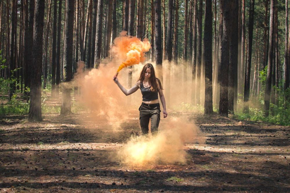 woman holding orange smoke flair near forest