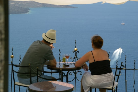 back view of man and woman sitting in front of terrace with sea view in Thera Greece