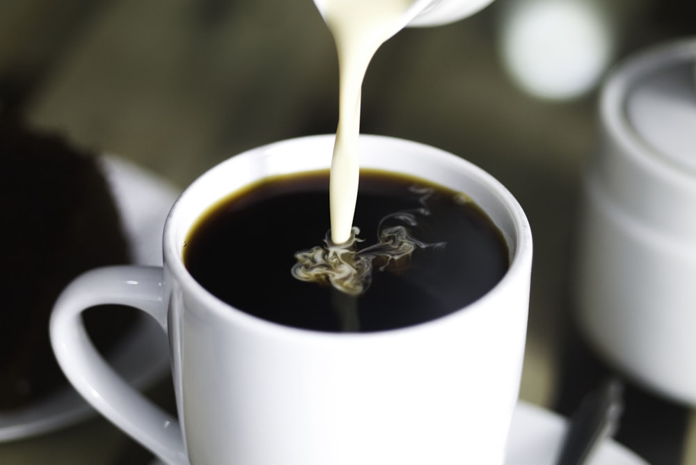 Café en taza de cerámica blanca mientras se vierte la leche