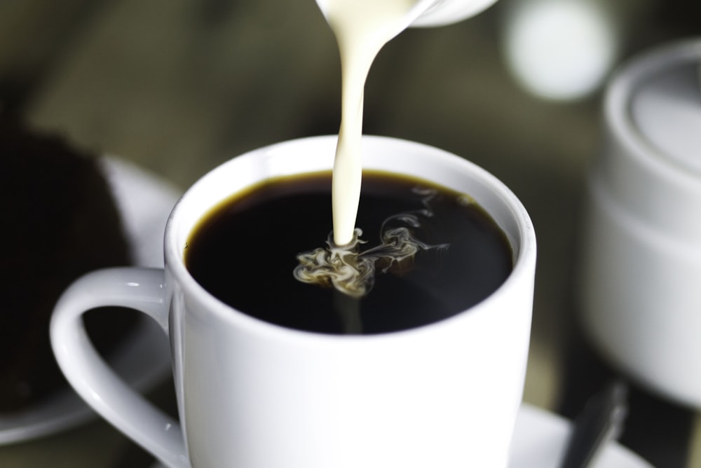Kaffee im weißen Keramikbecher beim Eingießen von Milch
