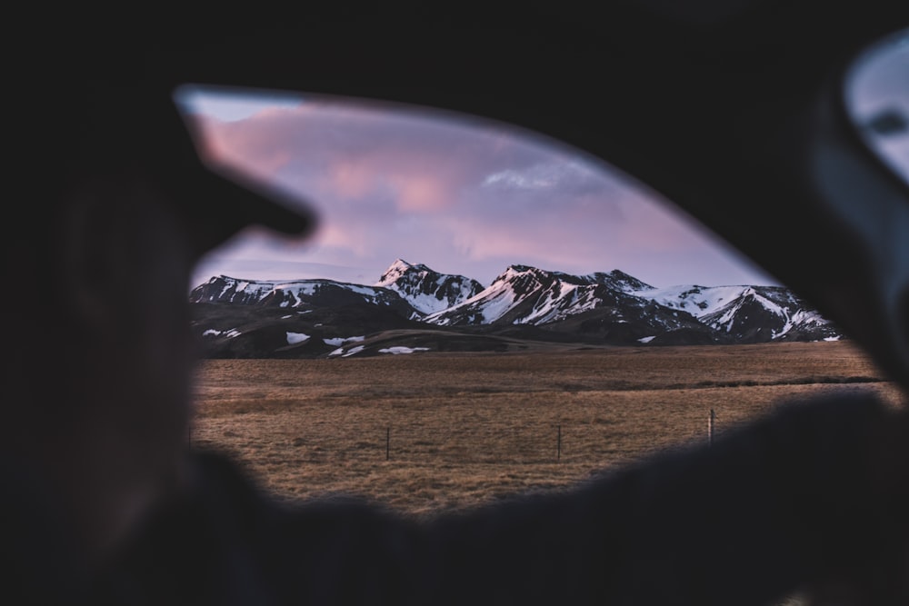 man sitting inside the car looking at snow capped mountain under white cloudy sky
