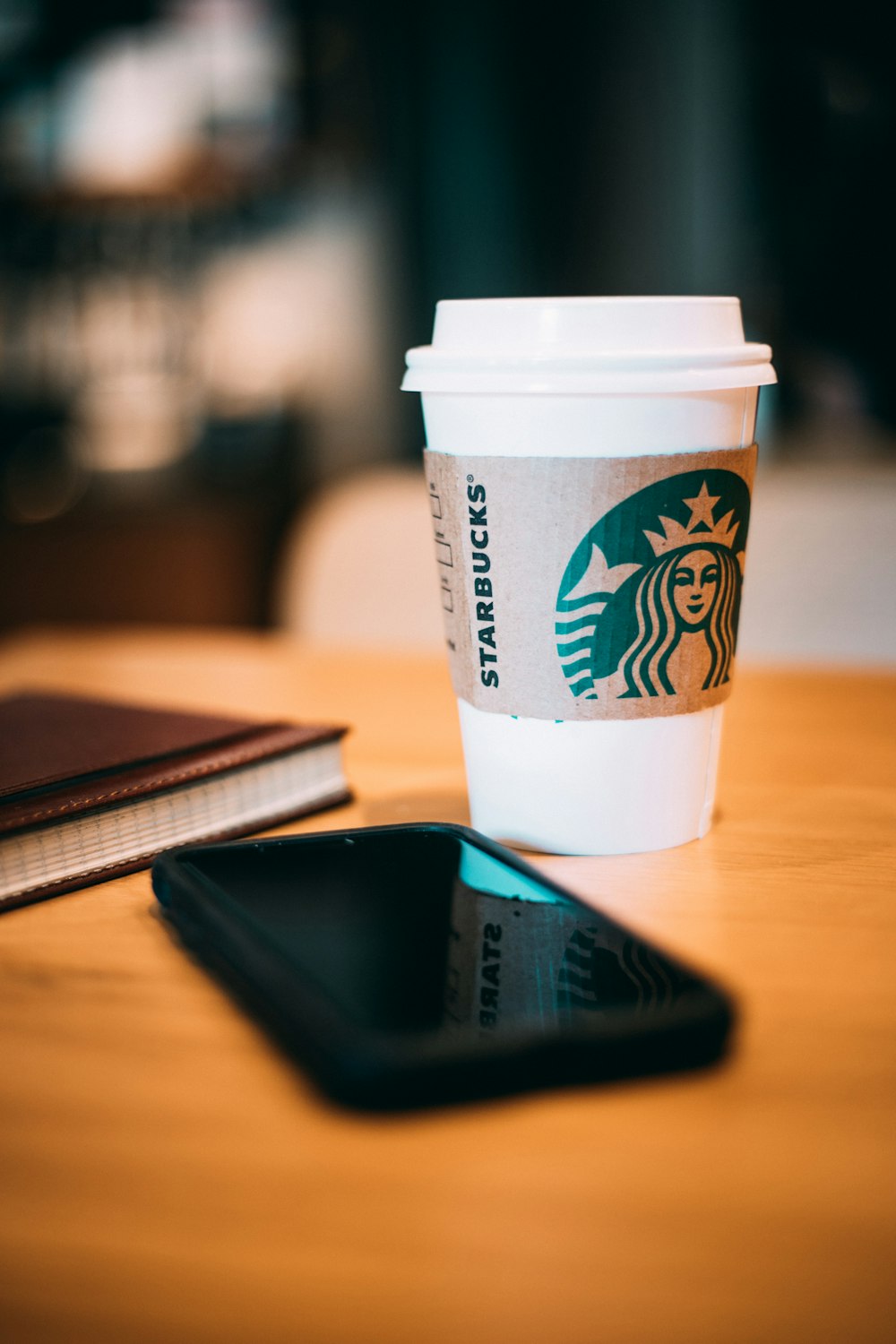smartphone preto ao lado de um copo Starbucks branco