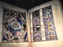 An illuminated manuscript featuring a detailed illustration of a figure surrounded by intricate patterns, along with a series of circular frames depicting various scenes. The imagery displays rich colors and fine craftsmanship, with Gothic text accompanying the artwork.