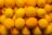 A large pile of fresh oranges with bright orange and yellow hues. The fruits are displayed closely together, showcasing their rough and textured surfaces under natural light.