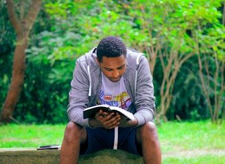 man sitting on concrete bench reading book
