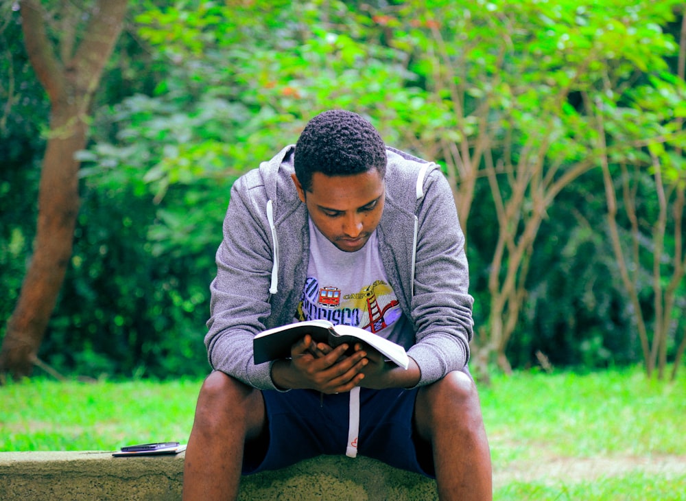 man sitting on concrete bench reading book