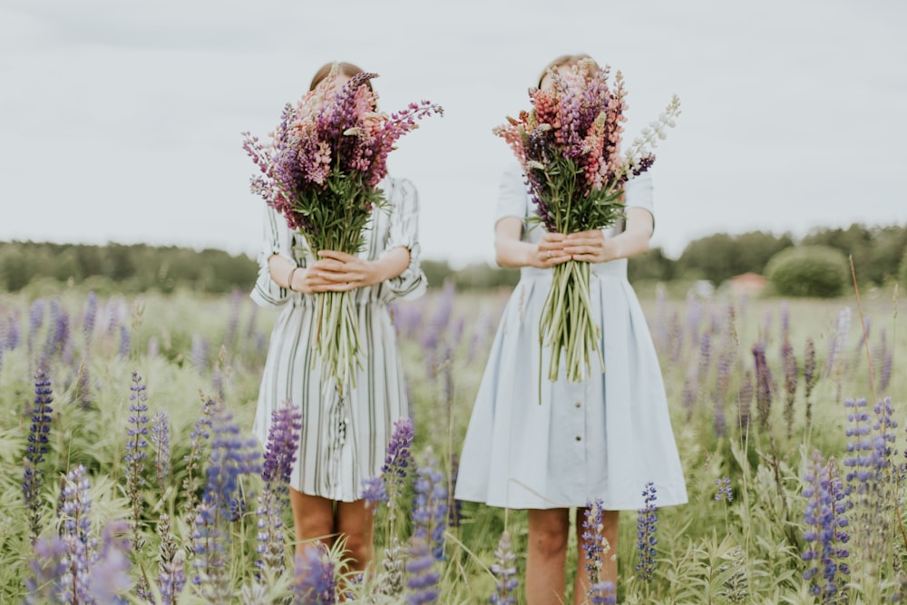 two woman holding pink petaled flowers