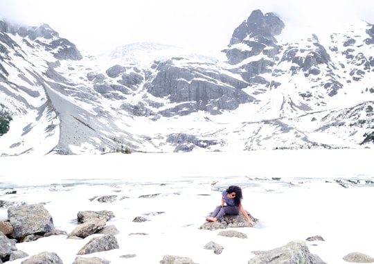 woman sitting on stone during winter at daytime in Joffre Lakes Trail Canada