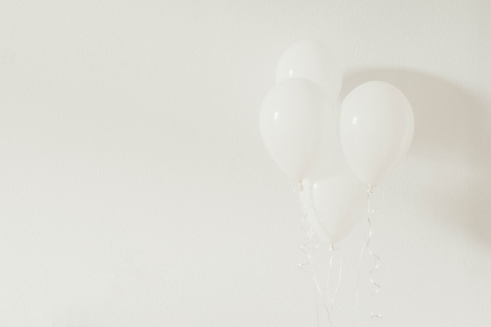 vier weiße Luftballons auf weißer Wand