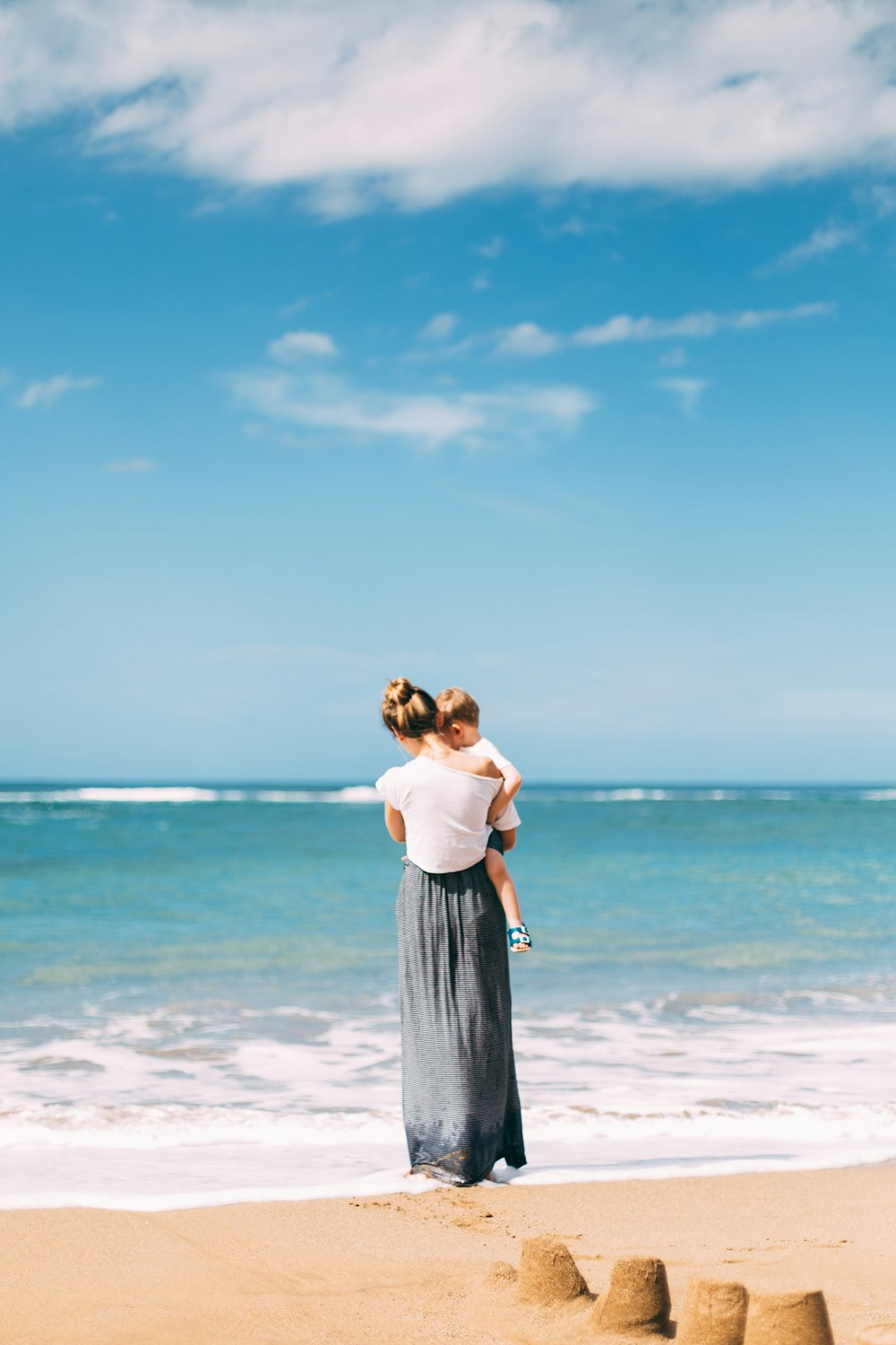 Frau trägt Kleinkind am Meeresufer