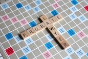 Wooden letter tiles spell out the words 'PROBATE' and 'LAWYER' on a Scrabble board. The board features a grid with colored squares marked with different point values such as 'Double Word Score' and 'Triple Letter Score'.