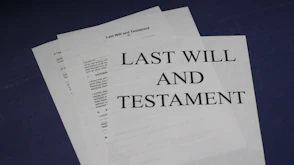 Close-up of hands signing a will document with a trusted advisor nearby.