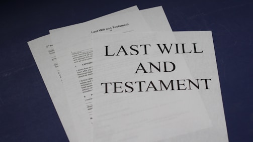 A stack of documents on a dark surface, with the top page clearly labeled 'Last Will and Testament' in bold letters. The documents appear to be legal papers, suggesting importance and formality.