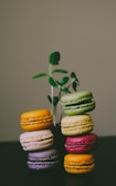 A stack of colorful mini cakes in yellow, green, and brown hues on a rustic wooden table.