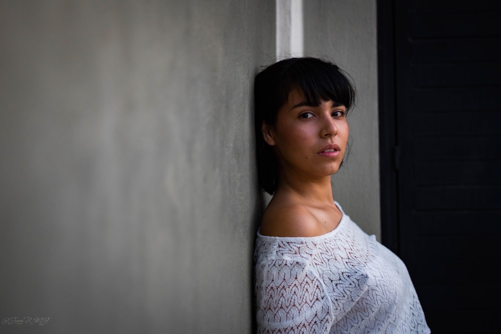 woman wearing white shirt leaning against gray wall