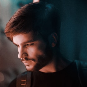 A well-groomed man admiring his shaped beard in the mirror under warm, moody lighting.
