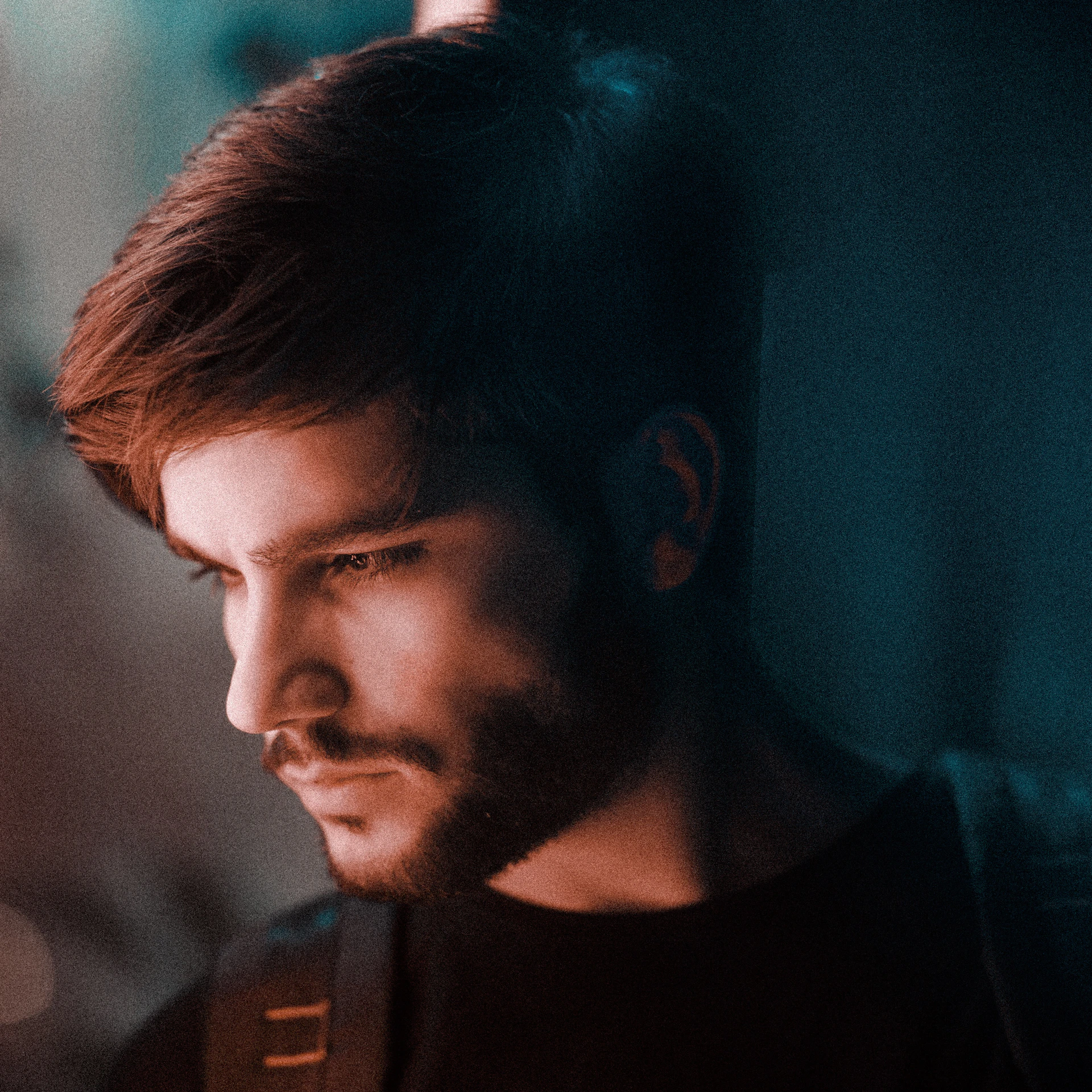 Close-up shot of a sharp, clean fade haircut with perfectly groomed beard, captured in moody lighting highlighting metallic barber tools.